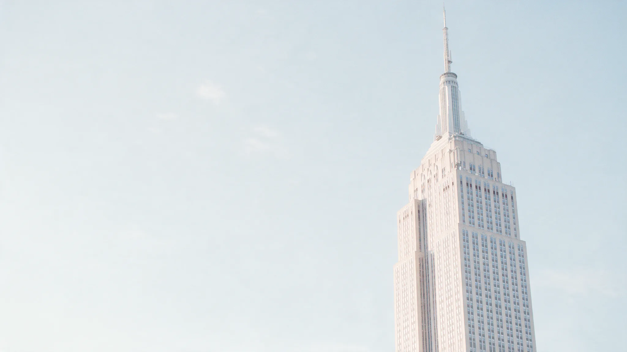 The spire of a stepped Art Deco tower against a pale morning sky